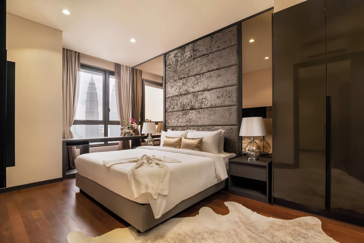 A modern hotel room with a large bed, a view of a city skyline, a large mirror, and a wooden floor.
