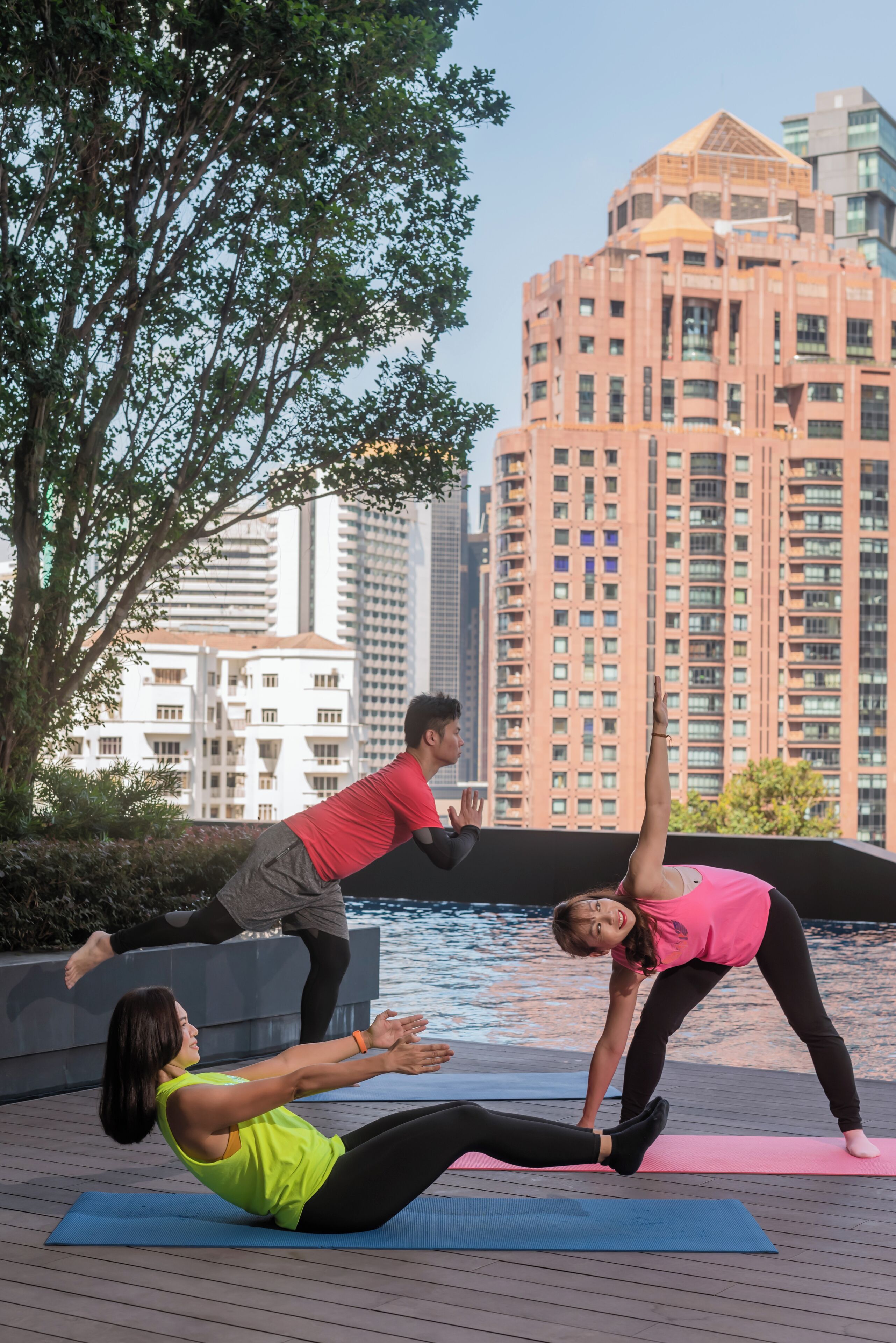 Un grupo de personas practicando yoga sobre esterillas junto a una orilla con edificios altos al fondo.