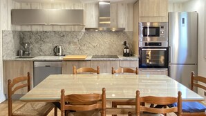 A modern kitchen with a marble countertop, stainless steel appliances, and a glass dining table with wooden chairs.