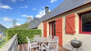 A deck with a table and chairs, a barbecue grill, and a house with red shutters.