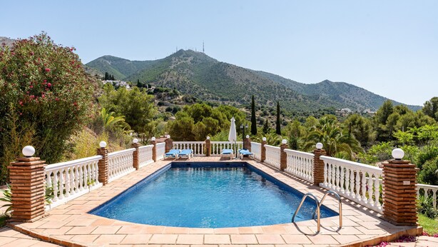 Una piscina rectangular con barandilla blanca, rodeada de pilares de ladrillo y una valla blanca.