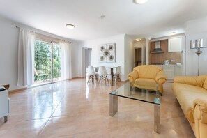 A modern living room with a glass coffee table, a yellow sofa, a dining area with white chairs, and a kitchen in the background.