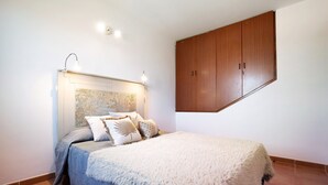 A bedroom with a bed, a headboard, a wooden wardrobe, and a wall-mounted light fixture. - Casa Aripauso with Shared Pool, Private Terrace, Sunset Views and Wi-Fi (Nuevo Hoirzonte)