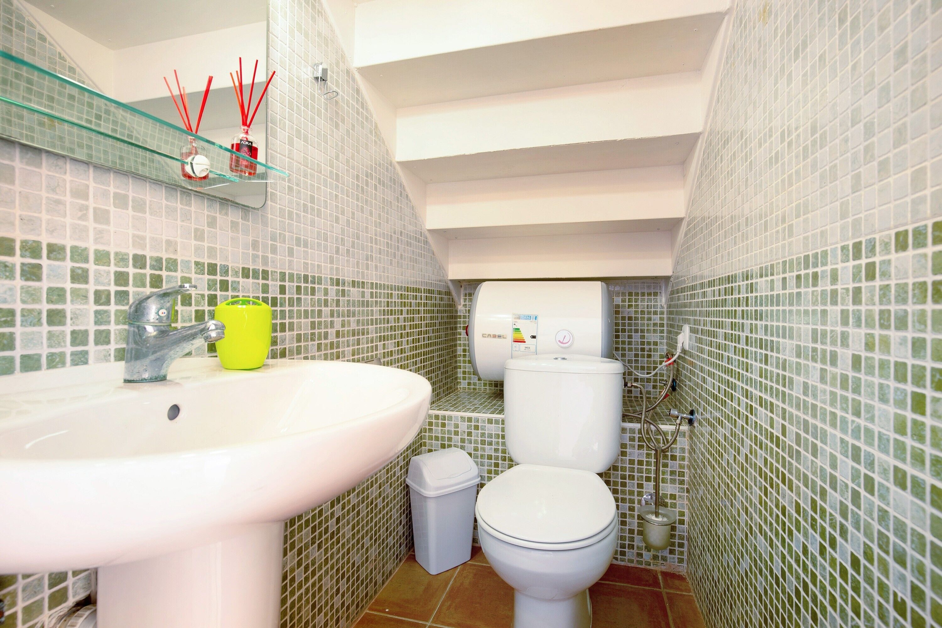 Un baño con lavamanos, inodoro y estante de vidrio con espejo.