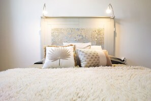 A bed with fluffy white bedding, a decorative headboard with a textured pattern, and two bedside lamps.