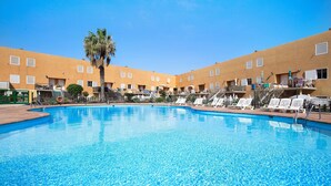 A swimming pool with lounge chairs and a palm tree, surrounded by a building with balconies. - Casa Aripauso with Shared Pool, Private Terrace, Sunset Views and Wi-Fi (Nuevo Hoirzonte)
