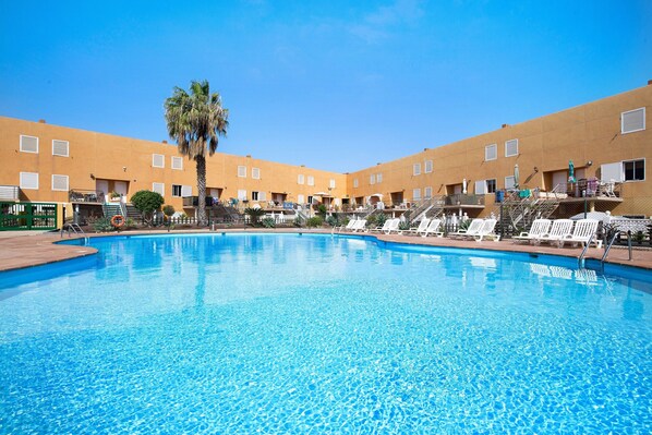 A swimming pool with lounge chairs and a palm tree, surrounded by a building with balconies.