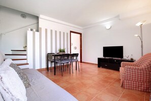 A living room with a sofa, a dining table with chairs, a TV, and a staircase.
