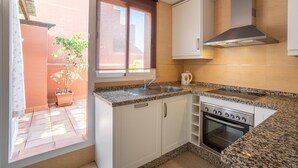 A kitchen with white cabinets, a stove, a sink, and a window overlooking a courtyard.