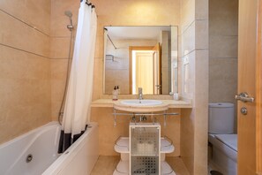 Et badeværelse med badekar, håndvask, spejl og toilet.