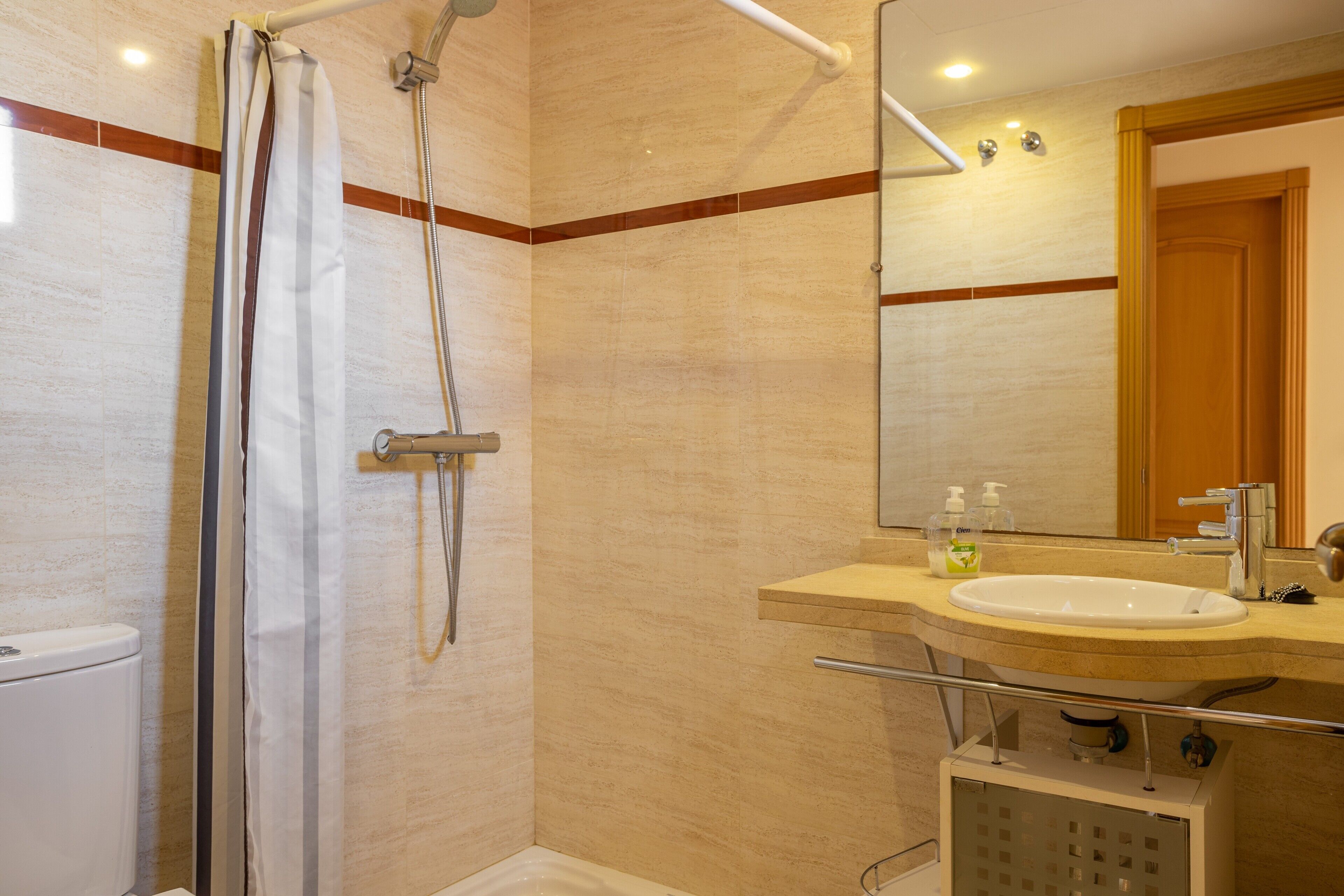 Ein Badezimmer mit Dusche, Toilette, Waschbecken und Spiegel.