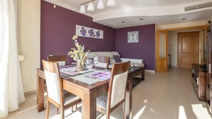 A dining area with a wooden table and chairs, a vase with flowers, and a clock on the wall.