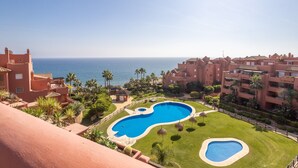 A resort with a large swimming pool, a view of the sea, and a well-maintained lawn.