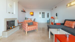 Ein Wohnzimmer mit Kamin, einer Couch, einem Esstisch und einer Küchenzeile im Hintergrund.