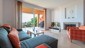 Ein modernes Wohnzimmer mit einer Couch, einem roten, gemusterten Sessel, einem Fernseher und einem Kamin.