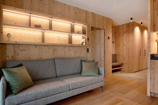 Un intérieur moderne avec un canapé gris, un lambris en bois et des étagères intégrées ornées d’objets décoratifs.