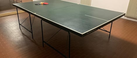 A ping pong table with a table tennis paddle and balls, a radiator, and a wall sign.