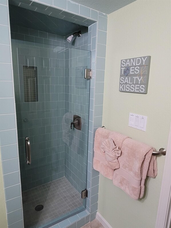 A bathroom with a glass-enclosed shower, a towel rack with a pink towel, and a wall sign with text.