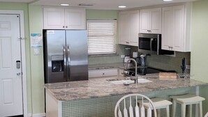 A kitchen with white cabinets, a stainless steel refrigerator, a microwave, and a sink. - Coastal Calm | Split level condo with ocean views (Port Aransas)