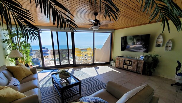A spacious living room with a large TV, comfortable seating, and a view of the ocean. - Coastal Calm | Split level condo with ocean views (Port Aransas)