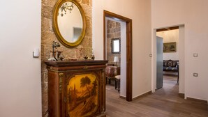 Un couloir doté d’un plancher en bois, d’un mur en pierre et d’un miroir placé au-dessus d’une armoire en bois ornée d’un tableau représentant un paysage.