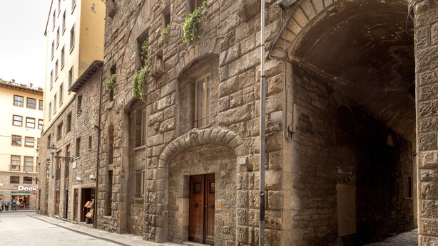 Ein historisches Steinhaus mit Holztür und Rundbogenfenstern, einem sichtbaren Hotelschild und einer gepflasterten Straße.