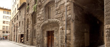 A historic stone building with a wooden door and arched windows, a visible sign for a hotel, and a cobblestone street.
