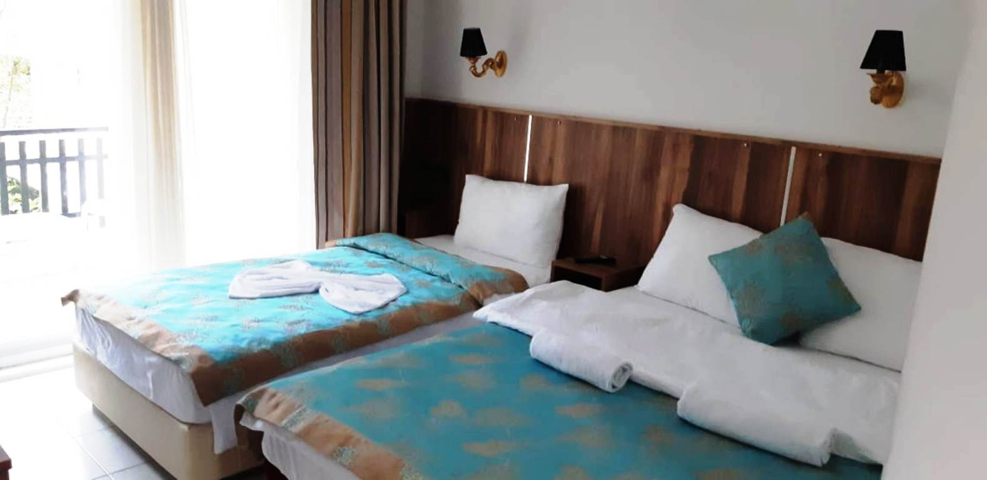 A hotel room with two beds, each with a wooden headboard, white pillows, and blue bedspreads. There are two wall-mounted lamps on either side of the beds.