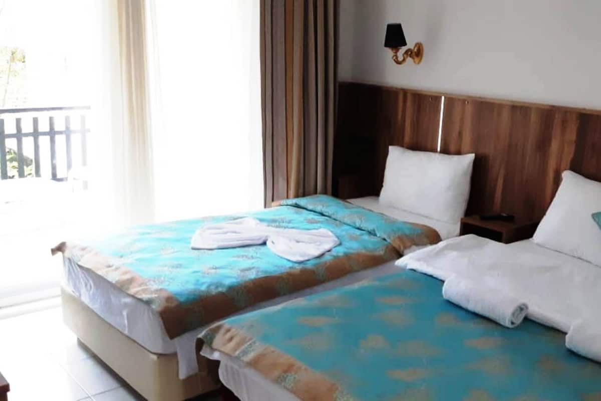 Habitación de hotel con dos camas, cada una con cabecero de madera, almohadas blancas y colchas azules. Hay dos lámparas de pared a cada lado de las camas.