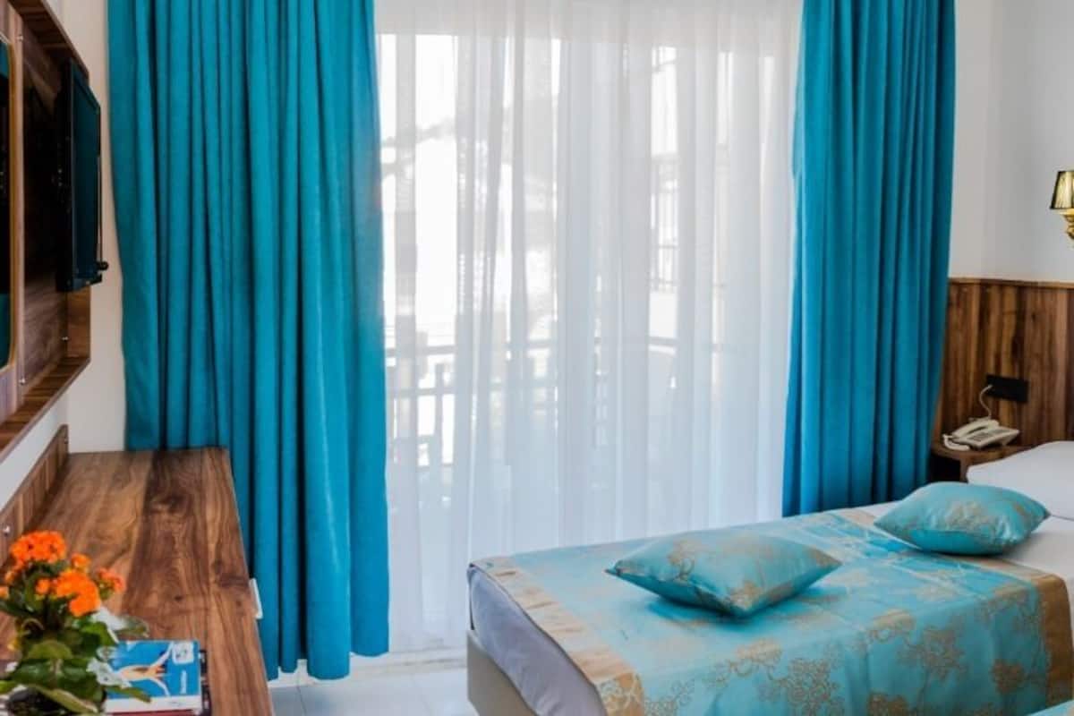 Habitación de hotel con dos camas, cabecero de madera, un espejo grande y una ventana con cortinas azules.