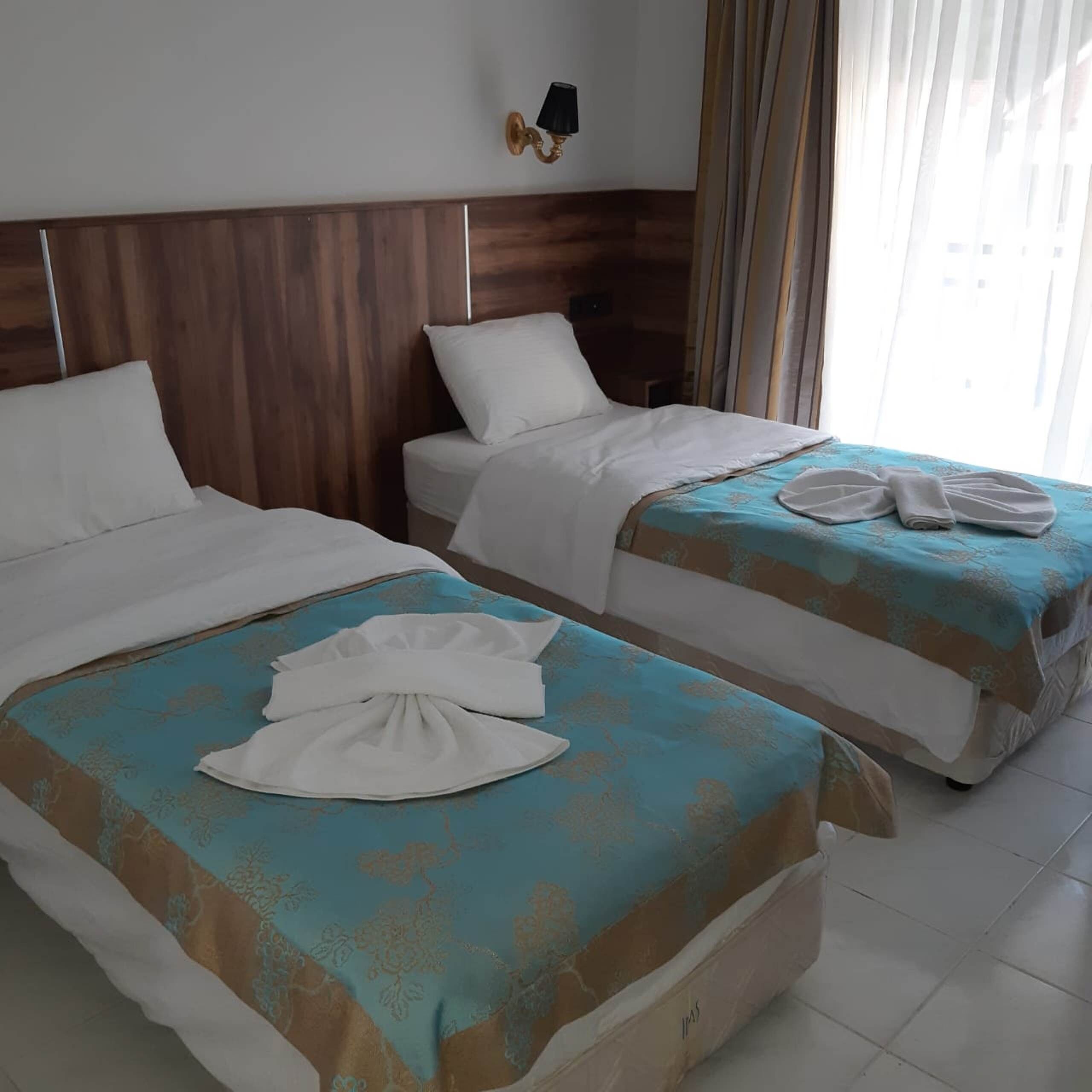 A hotel room with two beds, a wooden headboard, a wall-mounted lamp, and a window with curtains.