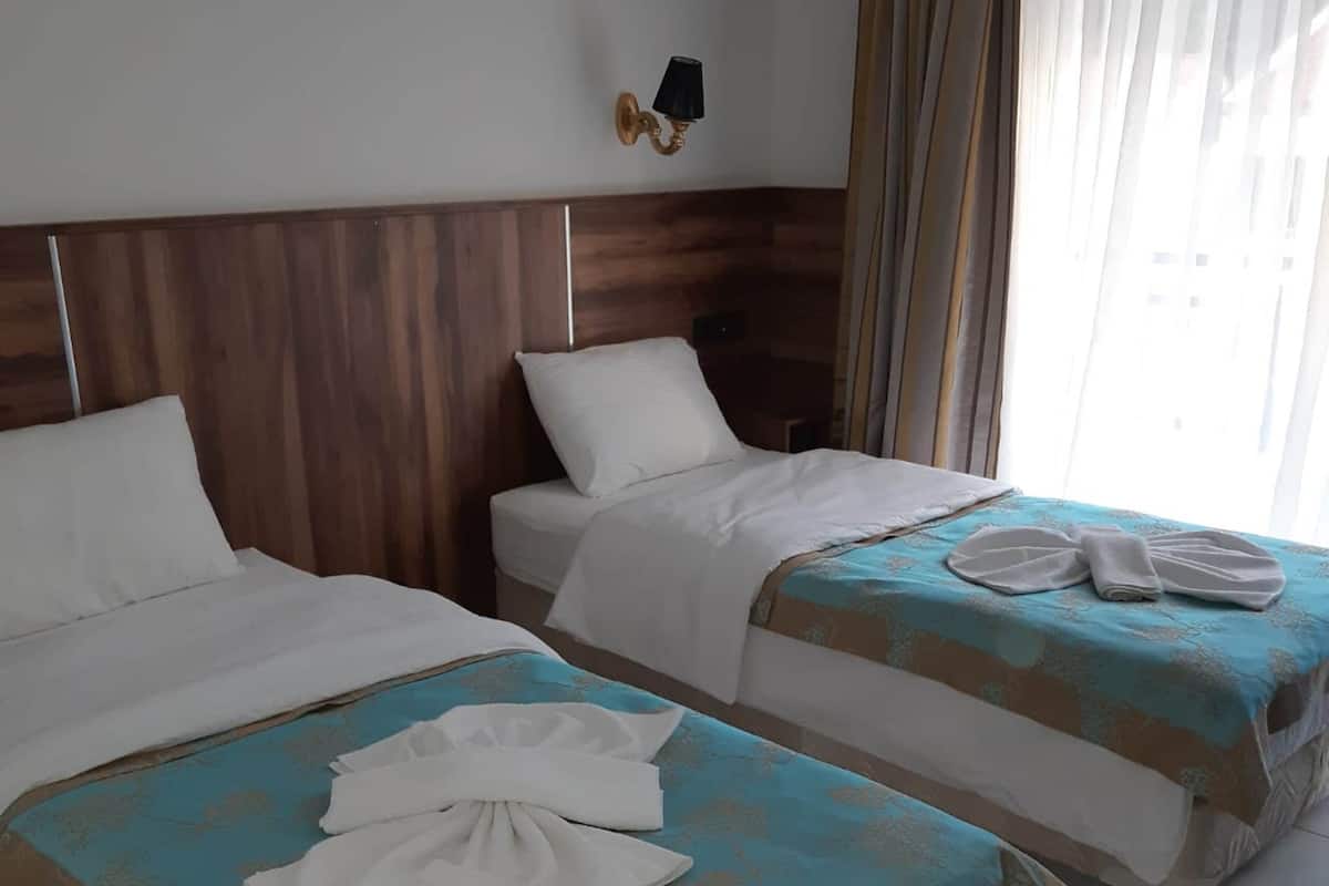 Habitación de hotel con dos camas, cabecero de madera, lámpara de pared y ventana con cortinas.