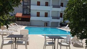 Relax by the clear pool surrounded by comfortable lounge chairs and tables, with the hotel building's balconies nearby.