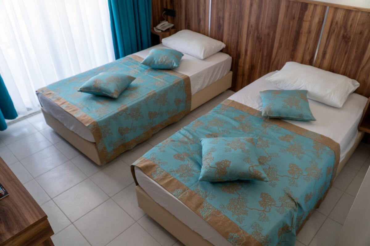 A hotel room with two single beds, each with a patterned bedspread and pillows.