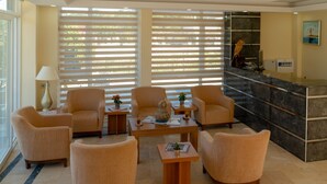 Vestíbulo con mostrador de recepción, zona de estar y ventanas amplias con persianas.