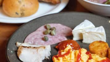 A breakfast plate with scrambled eggs, ham, croissants, and a glass of orange juice.
