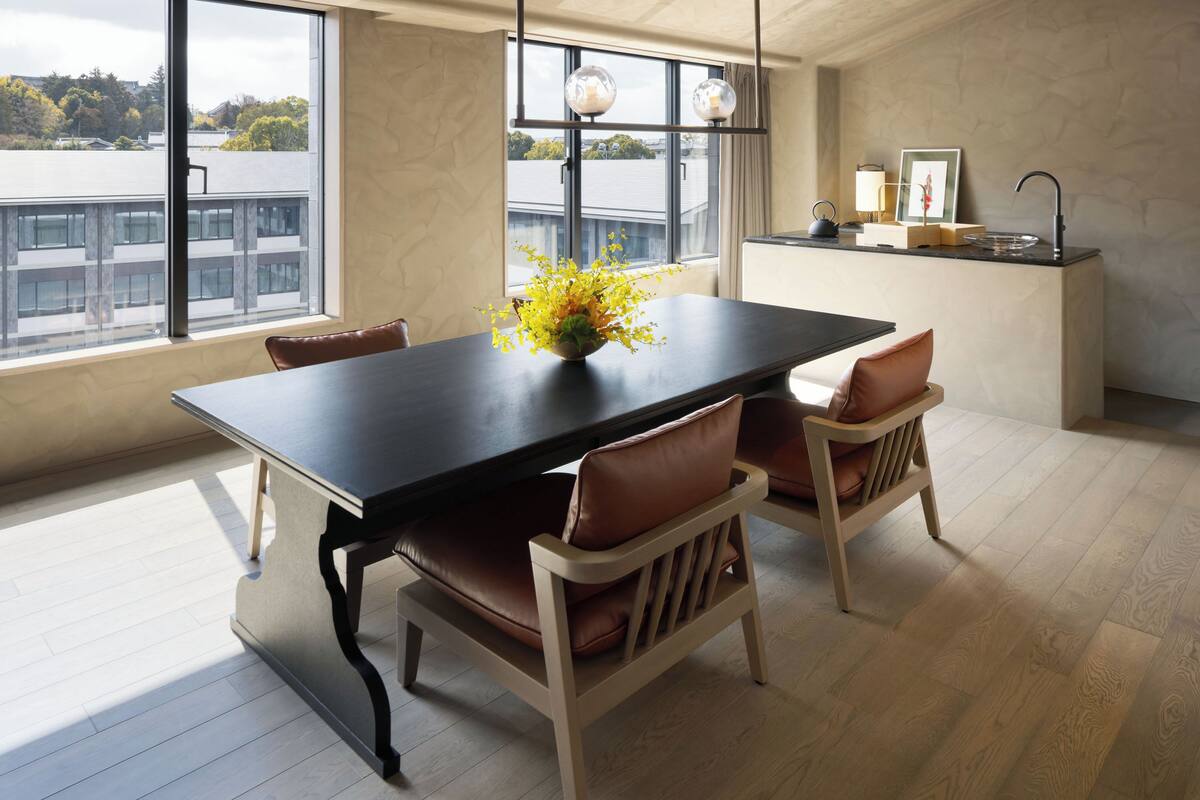 Ein Essbereich mit Tisch, Stühlen, einer Blumenvase, einem Fenster mit Aussicht und einer Küchenzeile mit Spüle und Arbeitsfläche.