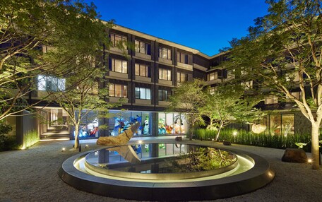 A modern building with a courtyard featuring a circular water feature, surrounded by trees and illuminated by ambient lighting.