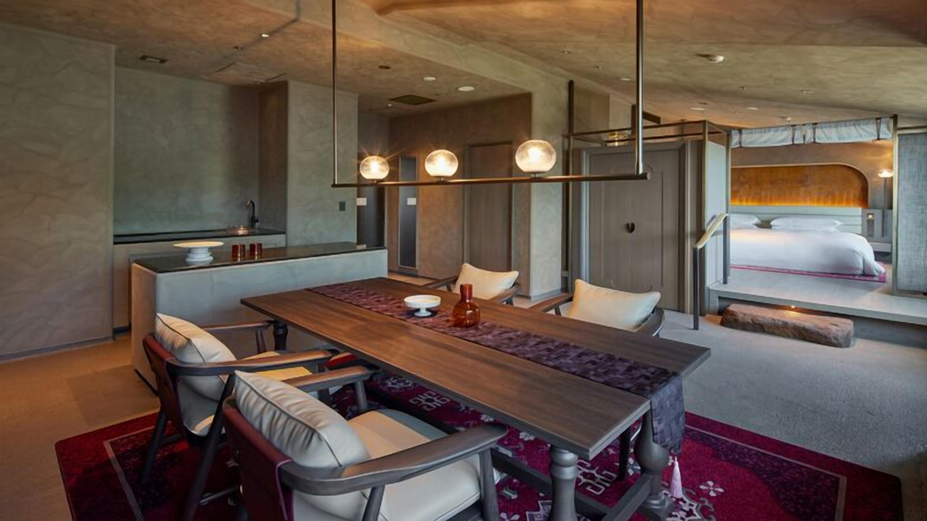 A modern hotel room with a dining area, a bed with a view, and a kitchenette.