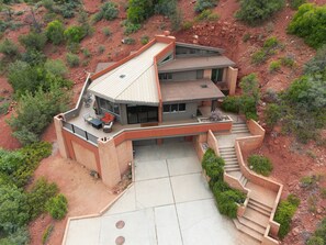 A modern two-story house with a large deck, a covered patio, and a staircase leading to the main entrance.