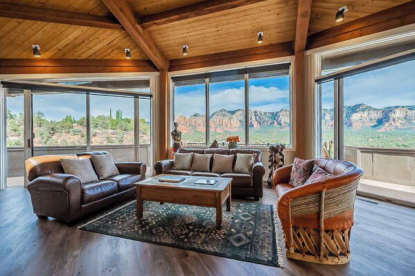 A spacious living room with a large window overlooking a mountainous landscape, furnished with leather sofas and a coffee table.