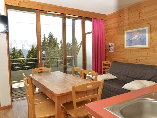 Un intérieur en bois comprenant une table à manger, des chaises, un canapé et une vue sur une montagne, visible à travers une grande fenêtre.