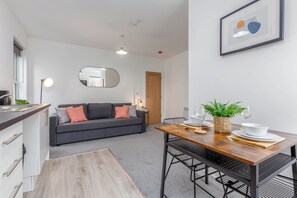 Ein modernes Wohnzimmer mit einer Couch, einem Esstisch mit Stühlen, einem Couchtisch, einer Pflanze und einem gerahmten Bild an der Wand.