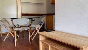 A compact living space with a wooden dining table and chairs, a small kitchenette, and a built-in wooden cabinet with drawers.