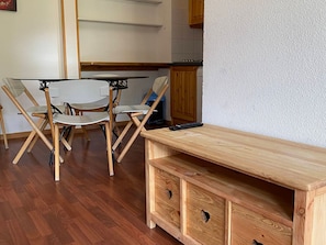 Um espaço de estar compacto com mesa e cadeiras de madeira, pequeno kitchenette e armário embutido de madeira com gavetas.