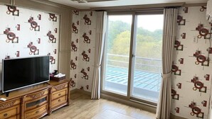 A room with a large TV on a wooden cabinet, patterned wallpaper, and a sliding glass door leading to a balcony. - Sokcho Haeoleumhouse (Sokcho)