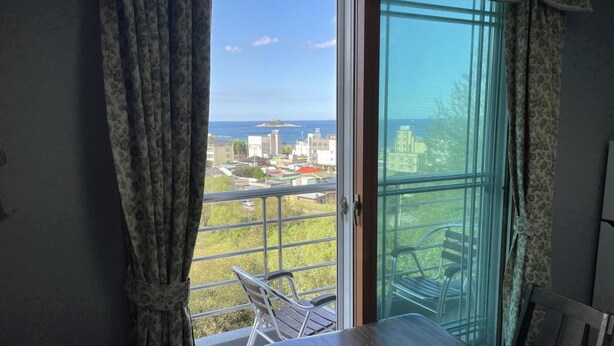 A balcony with a table and chairs, a view of buildings and a body of water. - Sokcho Haeoleumhouse (Sokcho)