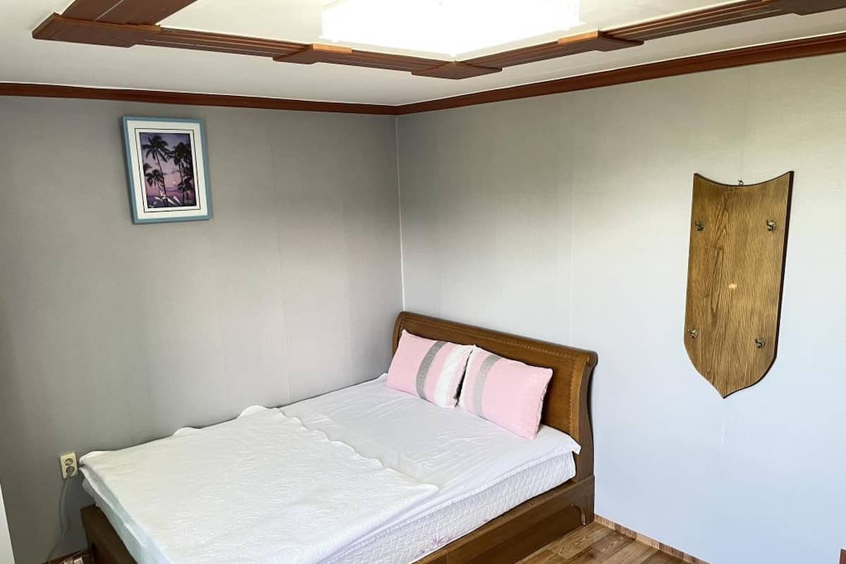 Un dormitorio con estructura de cama de madera, ropa de cama blanca y un cuadro colgado en la pared.