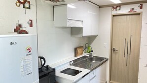 A compact kitchen with white cabinets, a microwave, a sink, and a wooden door. - Sokcho Haeoleumhouse (Sokcho)