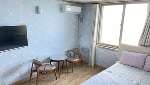 A bedroom with a bed, two chairs, a small table, an air conditioning unit, and a window with curtains. - Sokcho Haeoleumhouse (Sokcho)